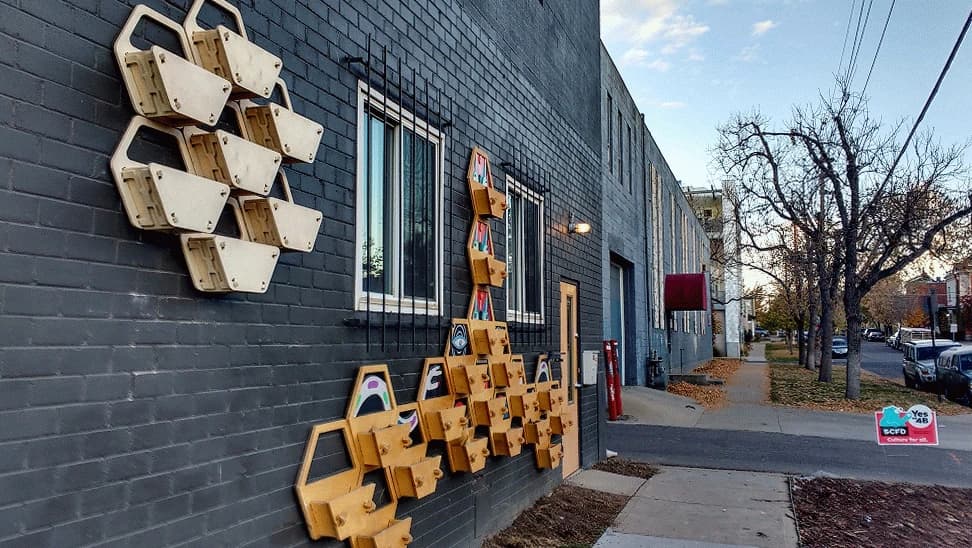 Hexagonal plywood wall planters mounted as two clusters on a dark brick building along a Denver sidewalk