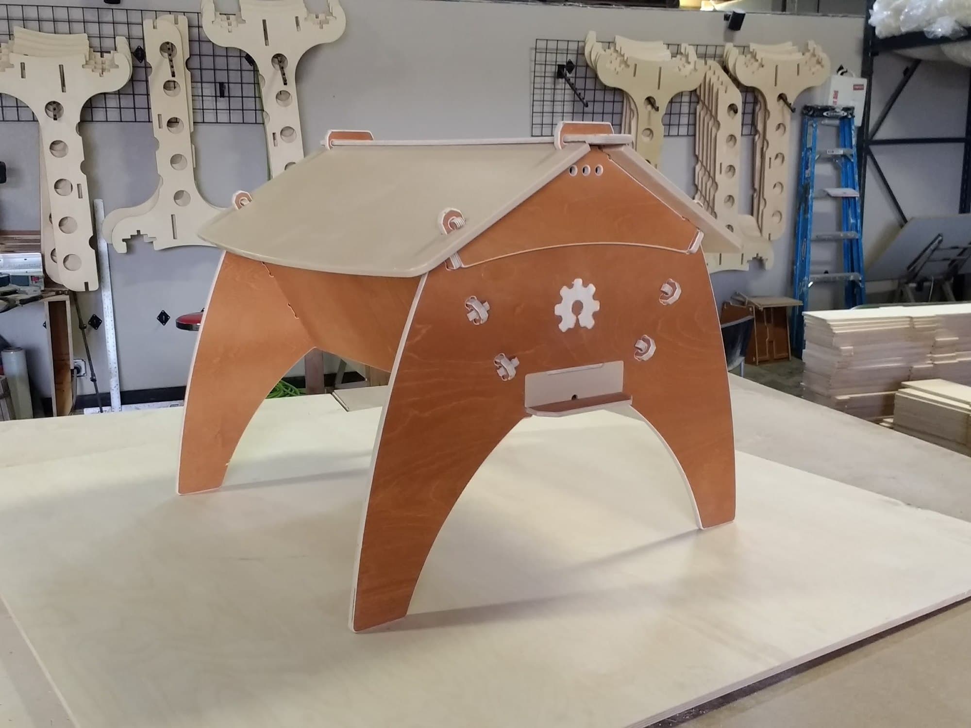 A finished top-bar beehive on the CNC bed, with cut plywood parts hanging on the wall behind it and stacked sheet stock to one side