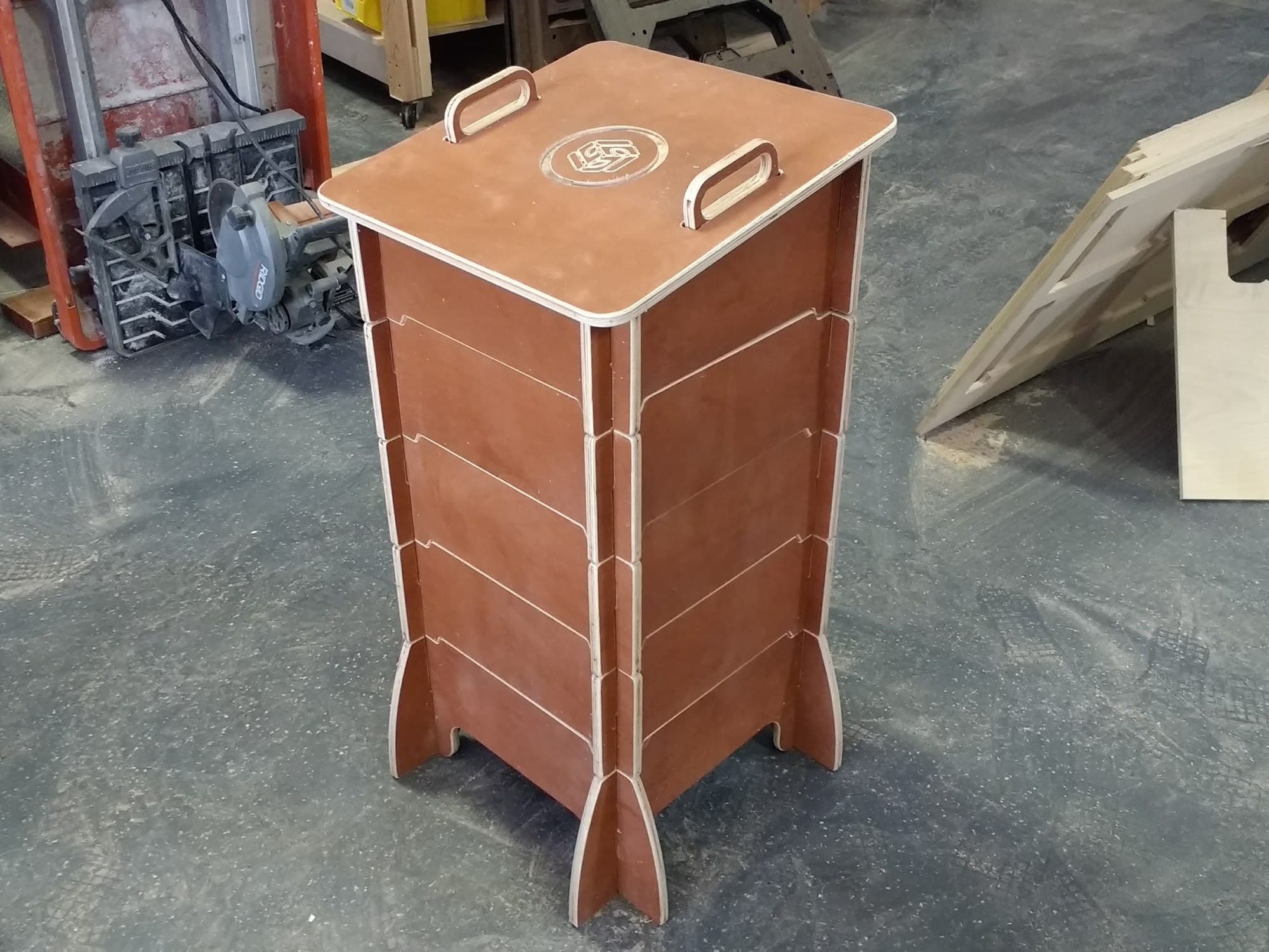A finished worm composter on the shop floor beside a saw and offcuts